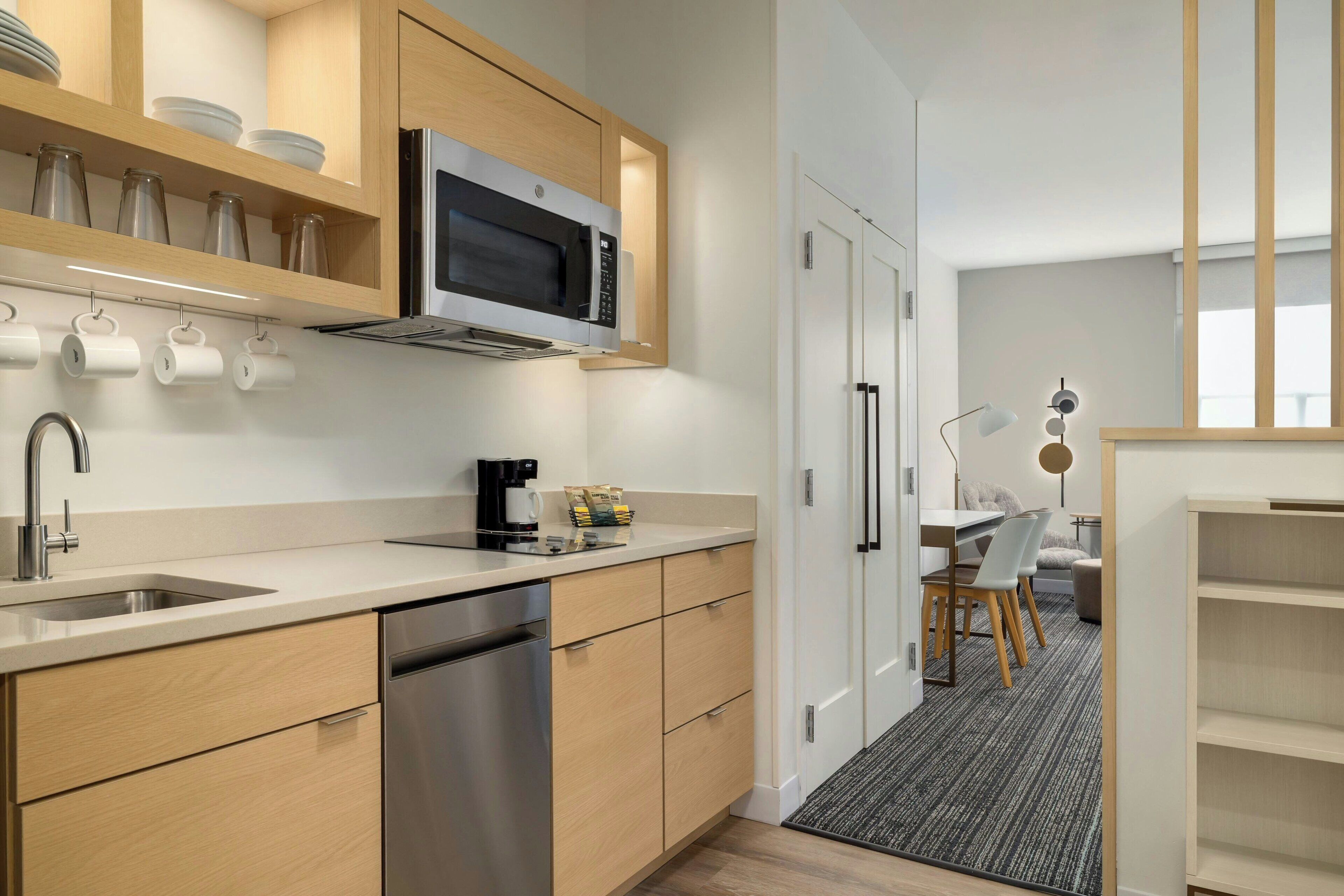 A modern kitchen with wooden cabinets, a stainless steel dishwasher, and a microwave. There is a coffee maker and a kettle on the counter.