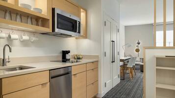 A modern kitchen with wooden cabinets, a stainless steel dishwasher, and a microwave. There is a coffee maker and a kettle on the counter.
