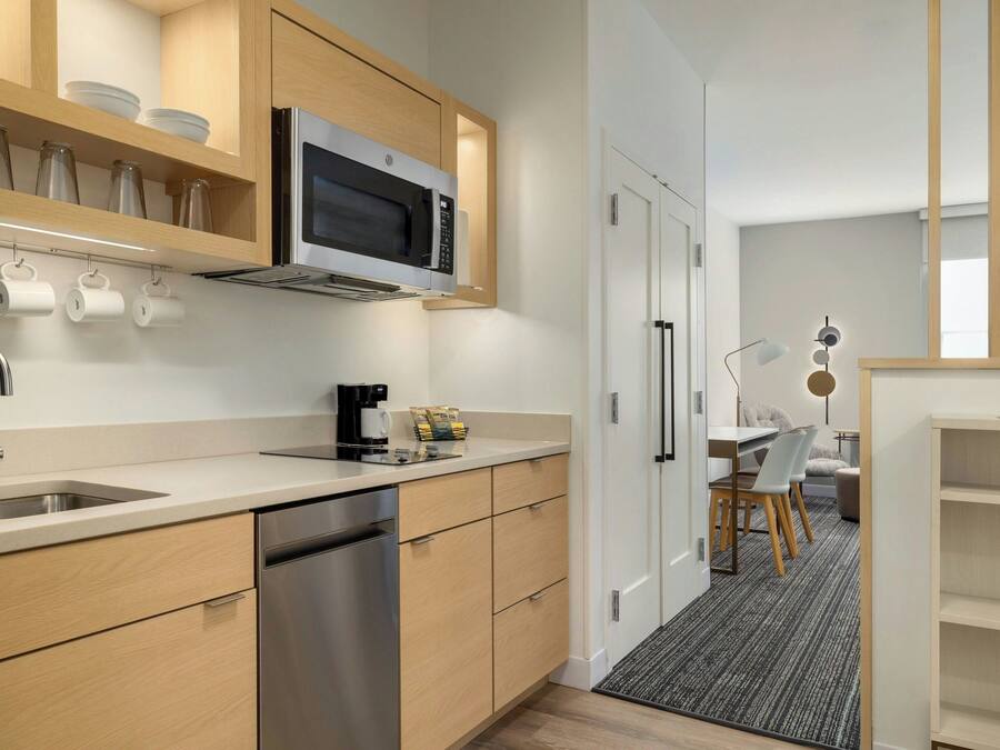 A modern kitchen with wooden cabinets, a stainless steel dishwasher, and a microwave. There is a coffee maker and a kettle on the counter.