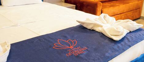 A hotel room with a neatly made bed, a blue towel with embroidered text, and an orange armchair.