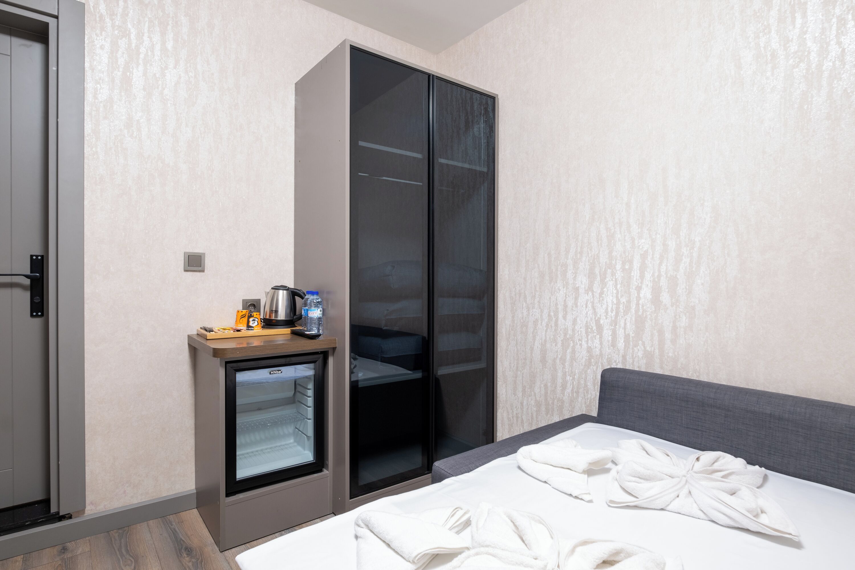 A hotel room with a bed, a minibar, a sliding closet, and a door.