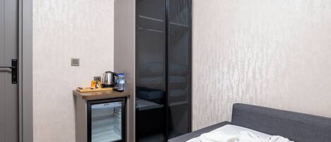 A hotel room with a bed, a minibar, a sliding closet, and a door.