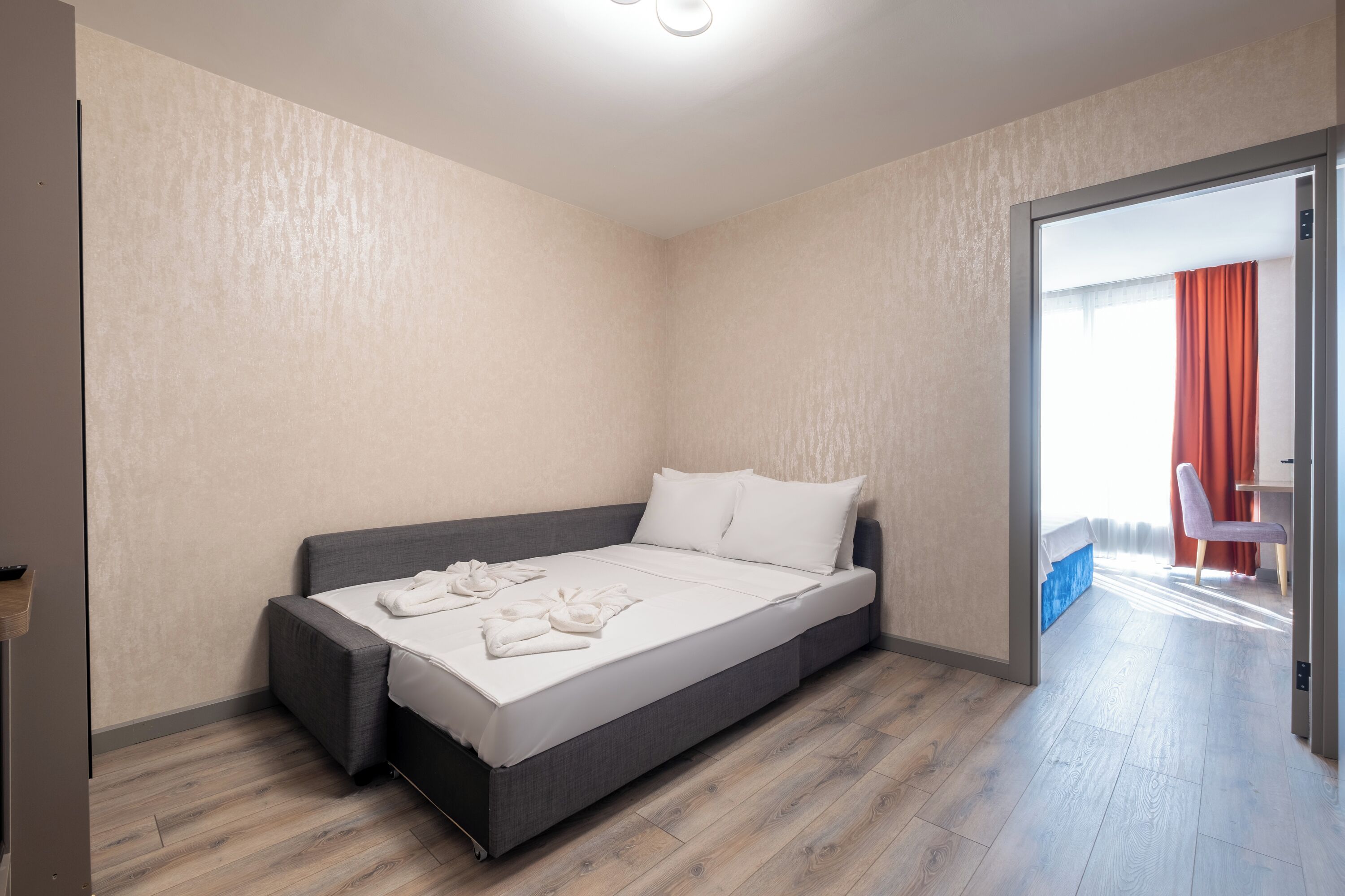 A modern bedroom with a single bed, a small seating area, and a view of the outside.
