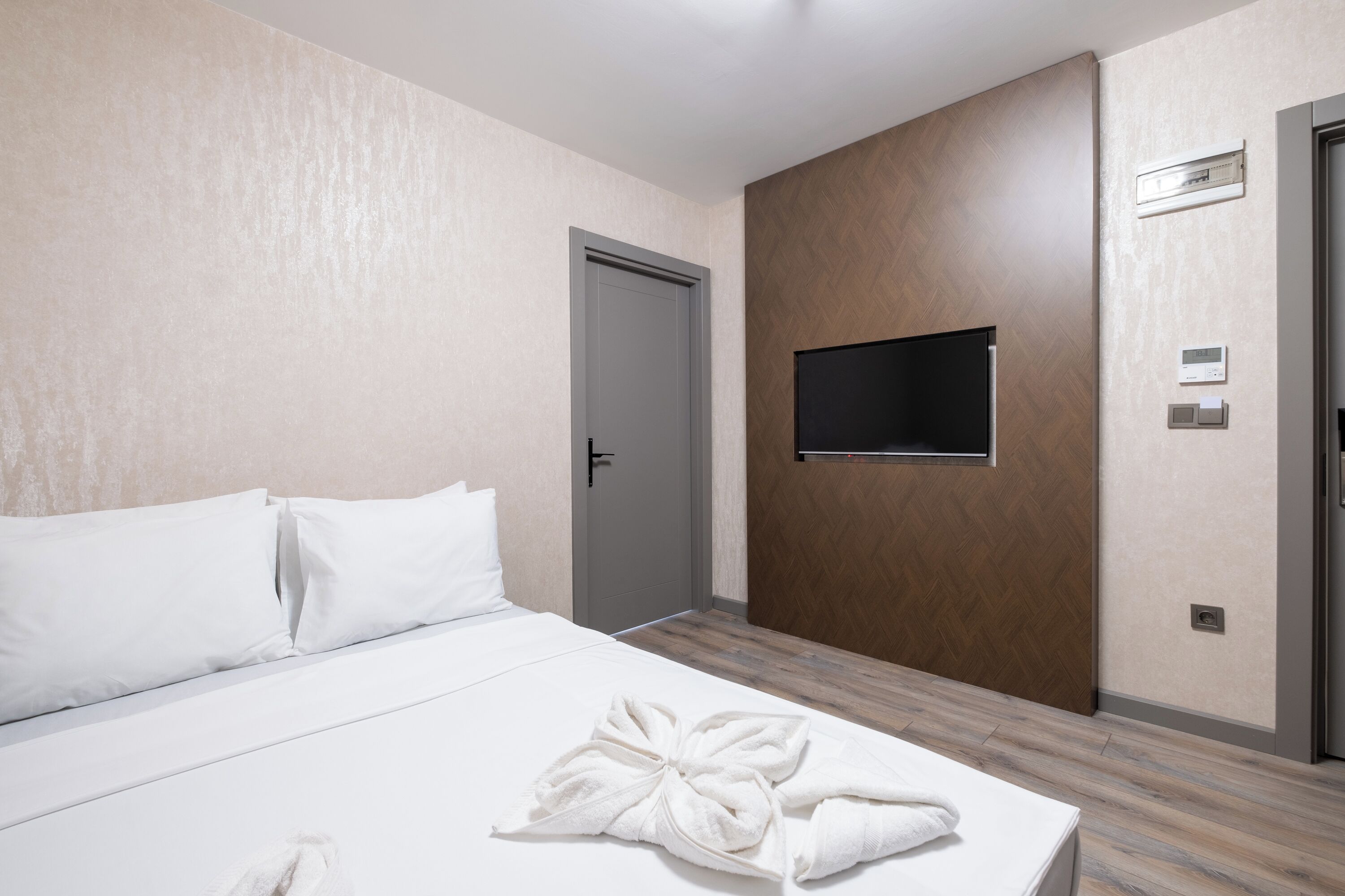 A hotel room with a bed, a flat-screen TV mounted on the wall, and a door.