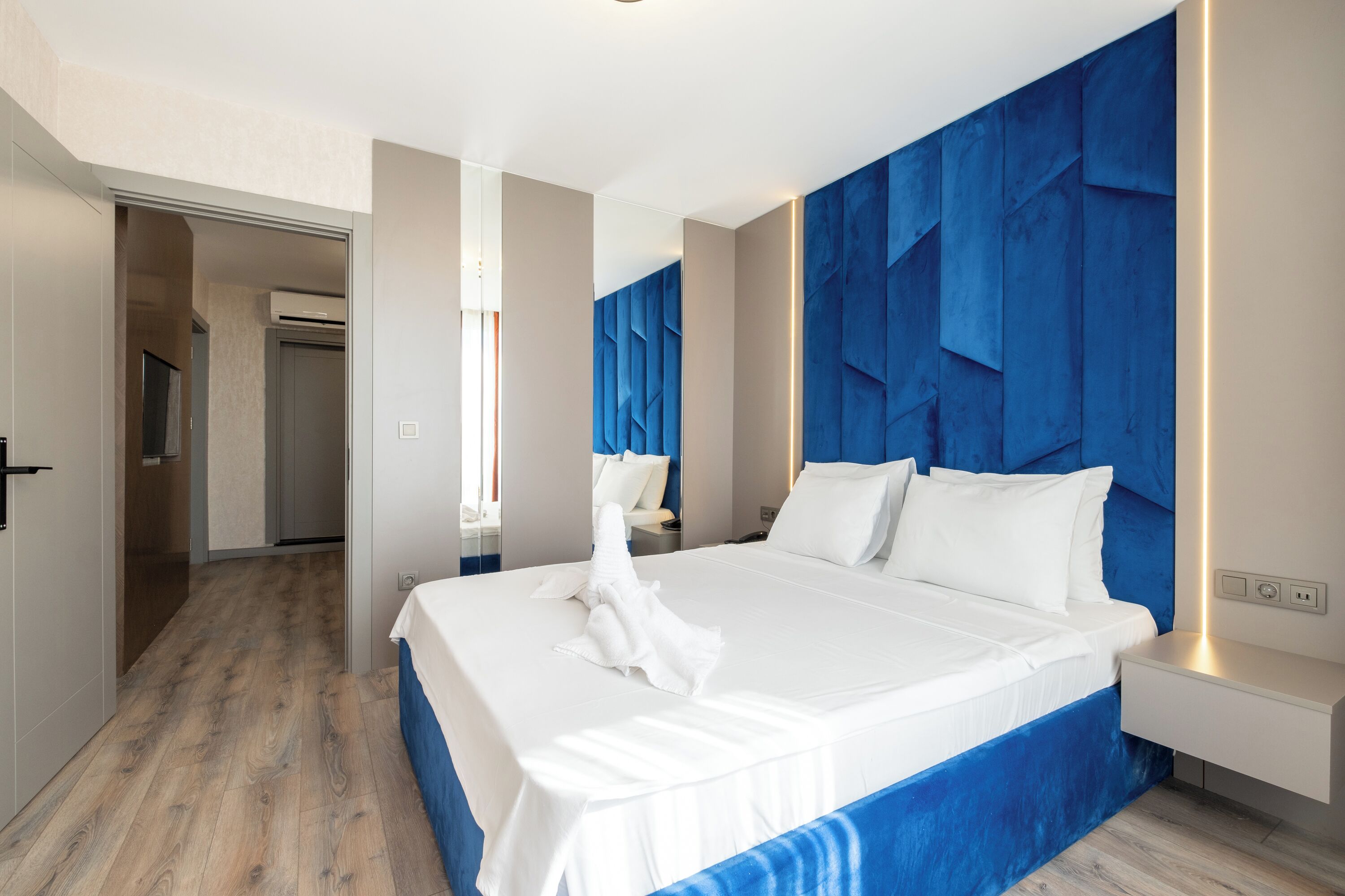 A modern hotel room with a large bed, a blue accent wall, and a bedside table with a lamp.