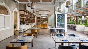 A modern restaurant with marble tables, hanging pendant lights, and a central bar area.