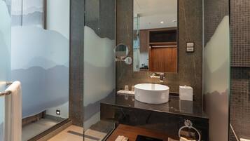 A modern bathroom with a large mirror, a round sink, and a wooden vanity.