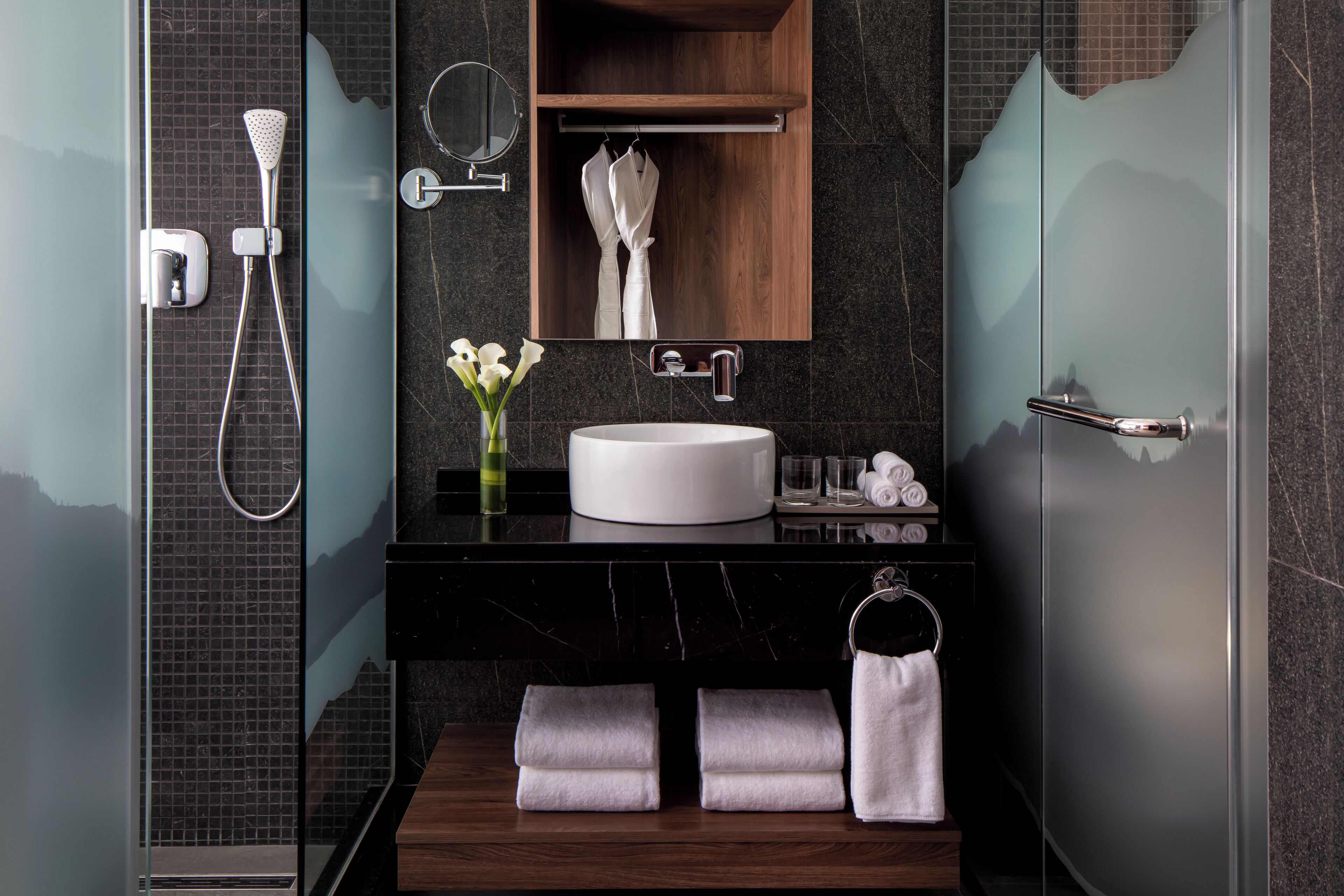 A modern bathroom with a glass shower enclosure, a wooden vanity with a white sink, and a mirror above the sink.