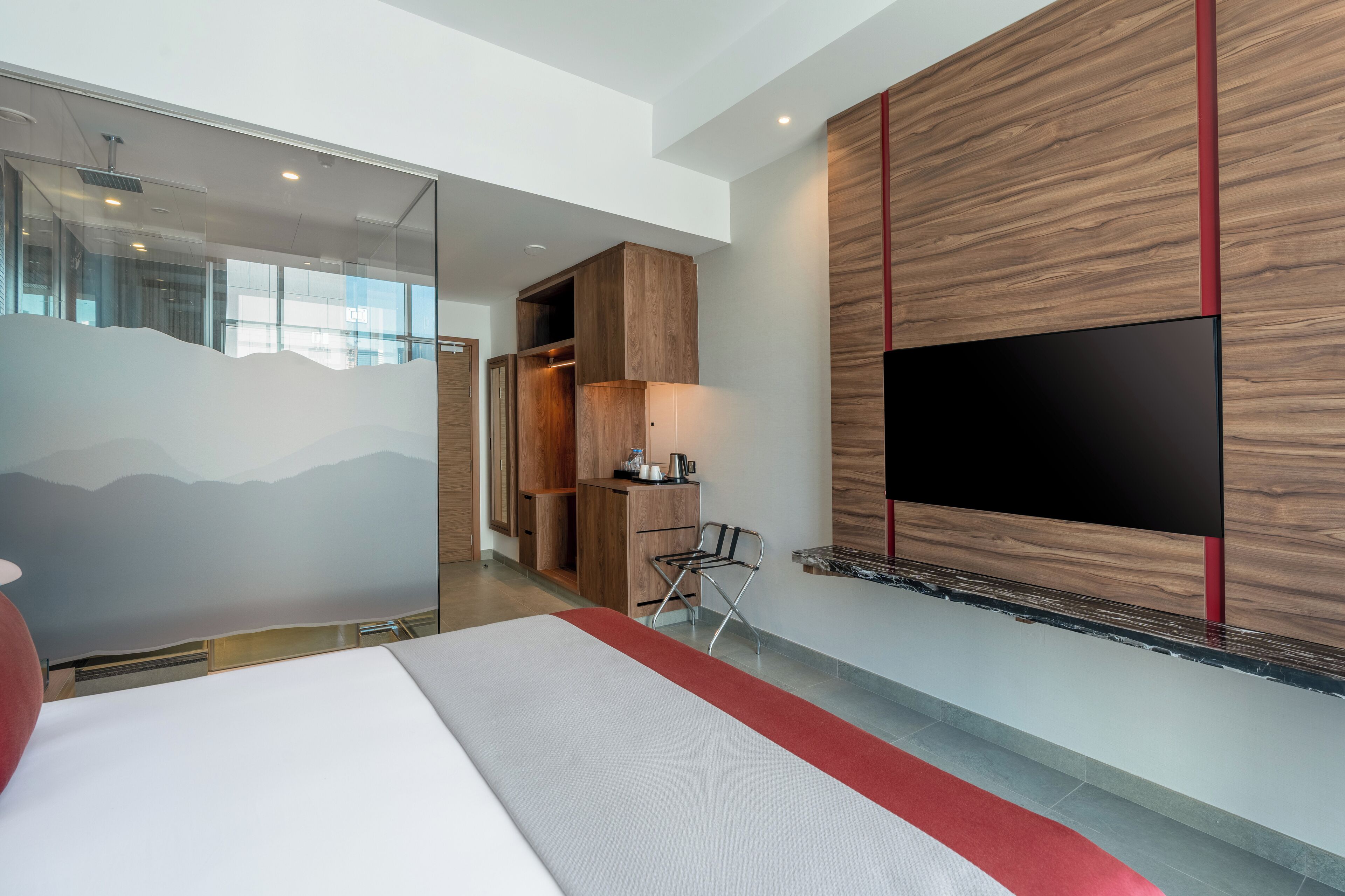Ein modernes Hotelzimmer mit einem großen Bett, einem flachbildfernseher an der Wand, einem Holzschrank und einem kleinen Schreibtisch mit Stuhl.