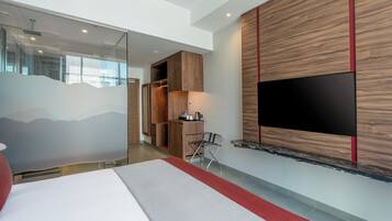 Ein modernes Hotelzimmer mit einem großen Bett, einem flachbildfernseher an der Wand, einem Holzschrank und einem kleinen Schreibtisch mit Stuhl.