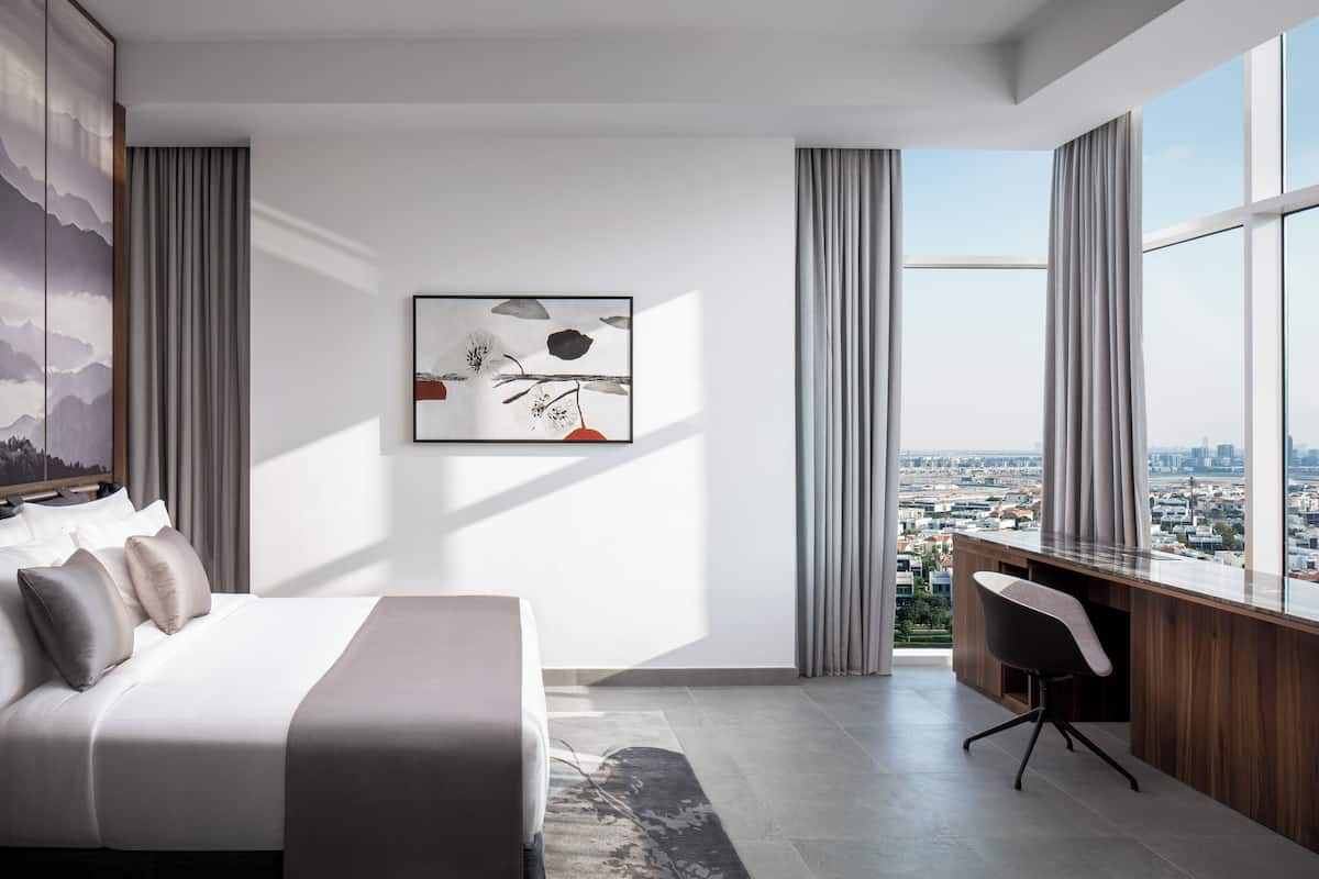 A modern hotel room with a large bed, a desk, and a city view.