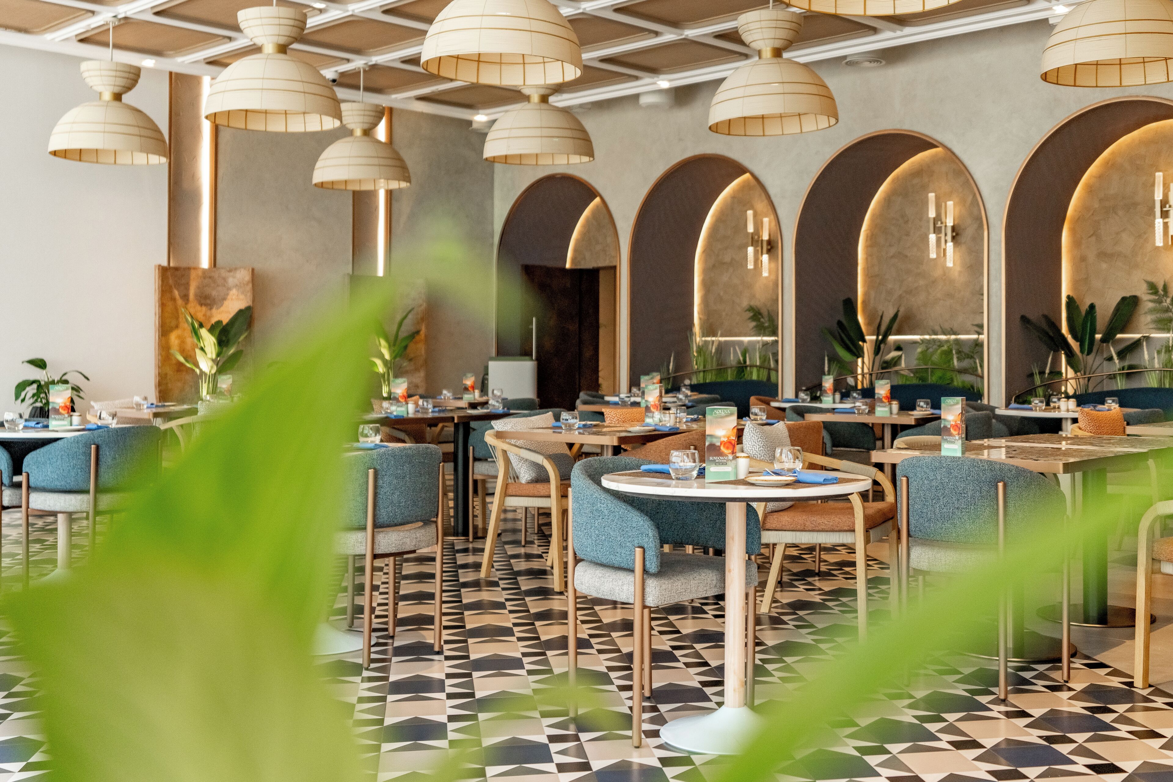 Interior de restaurante con varias mesas, sillas y lámparas colgantes.