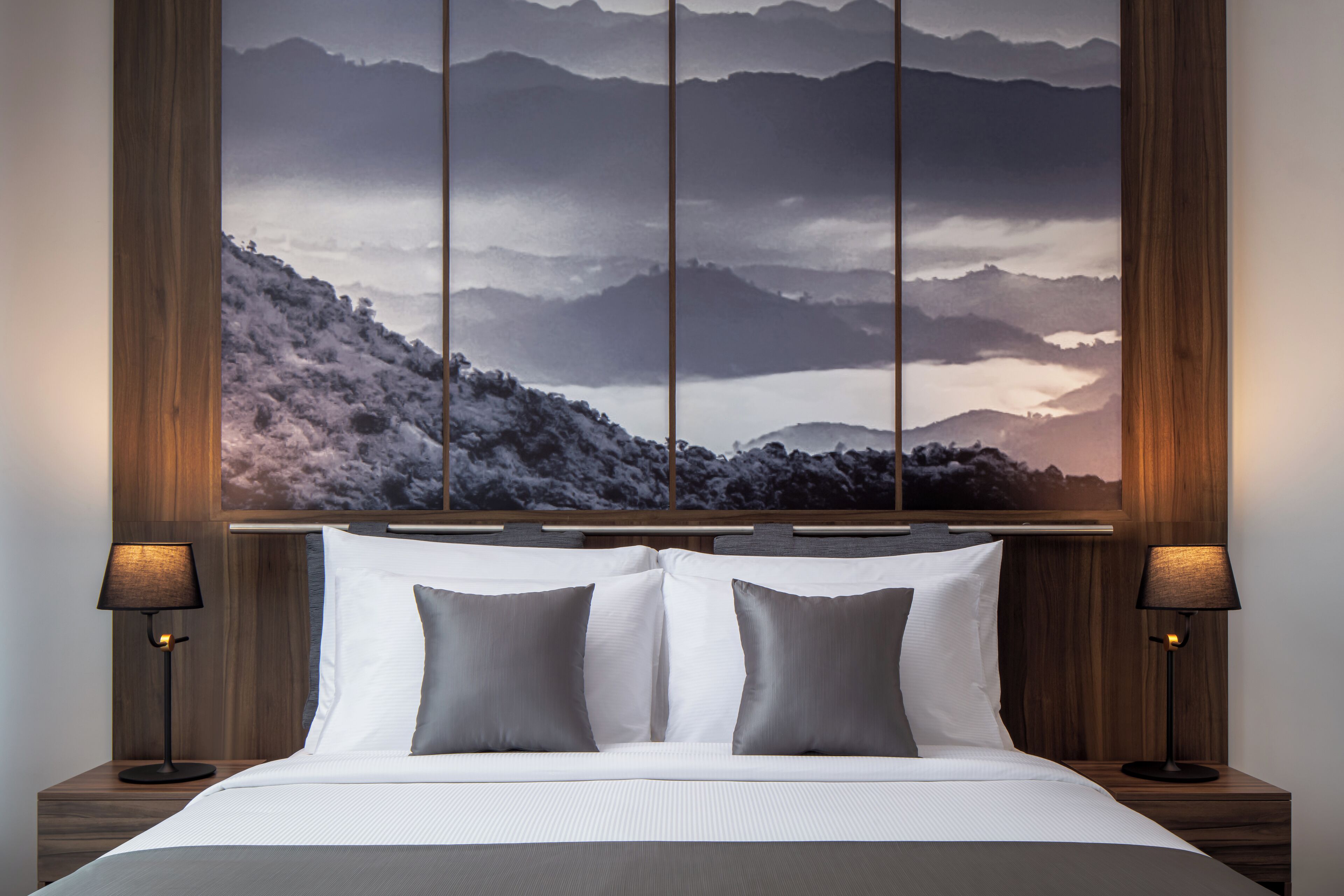 Une chambre d’hôtel avec un grand lit, deux lampes de chevet et une œuvre d’art accrochée au mur représentant un paysage montagneux.