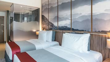 A hotel room with two beds, a large wall mural of mountains, and a glass partition.