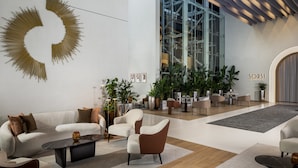 A modern interior with a white sofa, a black coffee table, and a brown armchair. There are potted plants and a large glass window. - Grand Millennium Business Bay (Dubai)