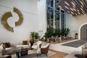Un interior moderno con un sofá blanco, una mesa de centro negra y un sillón marrón. Hay plantas en macetas y un amplio ventanal.