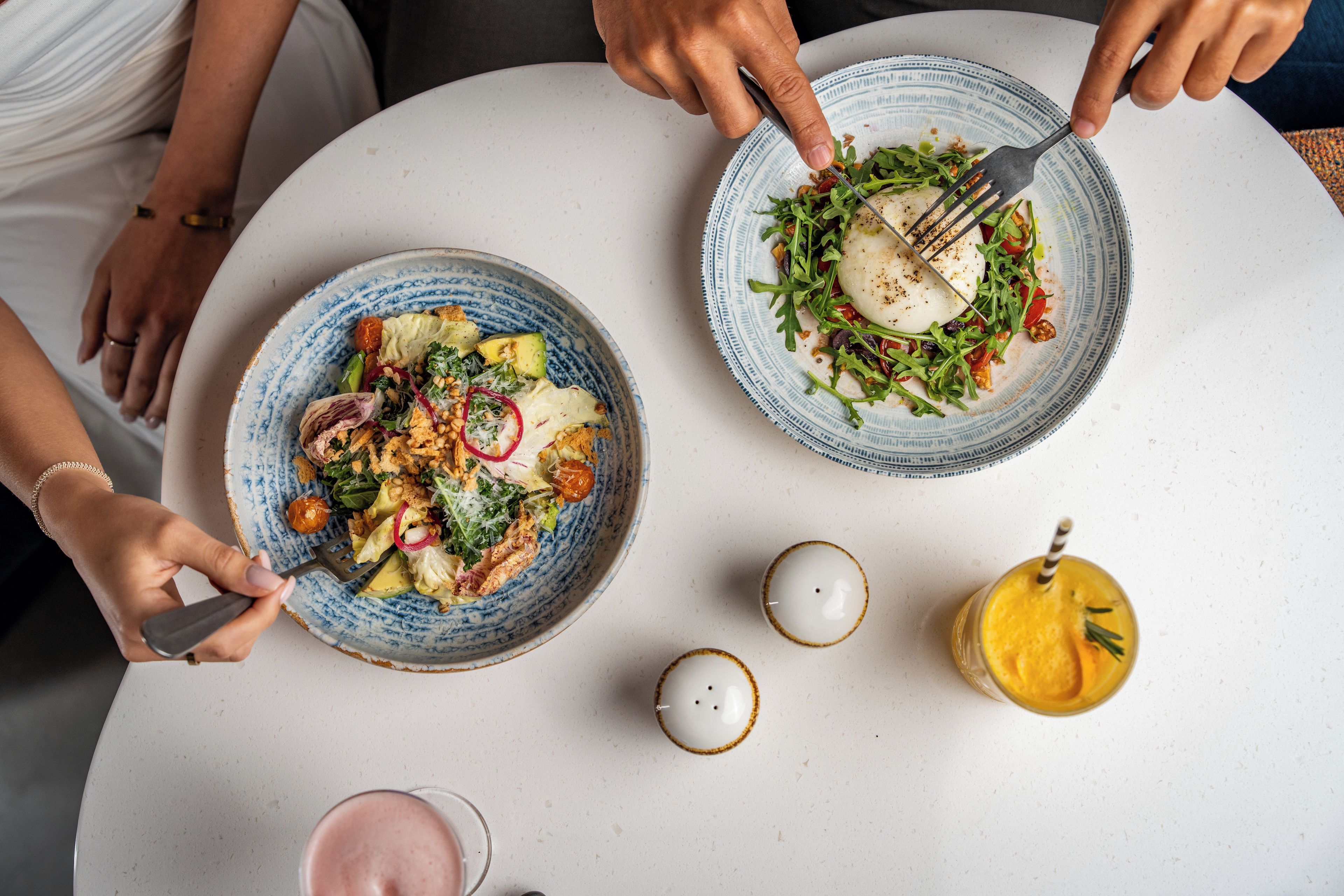 A dining table with two plates of food, a glass of drink, and two candles.
