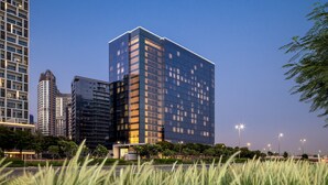 A modern high-rise building with a glass facade, surrounded by other tall buildings and a well-maintained park area. - Grand Millennium Business Bay (Dubai)