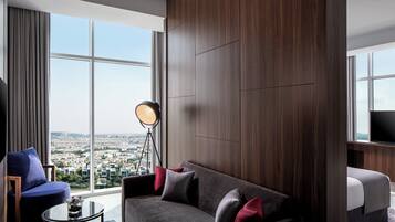 A modern hotel room with a large window, a sofa, a small table, and a floor lamp.