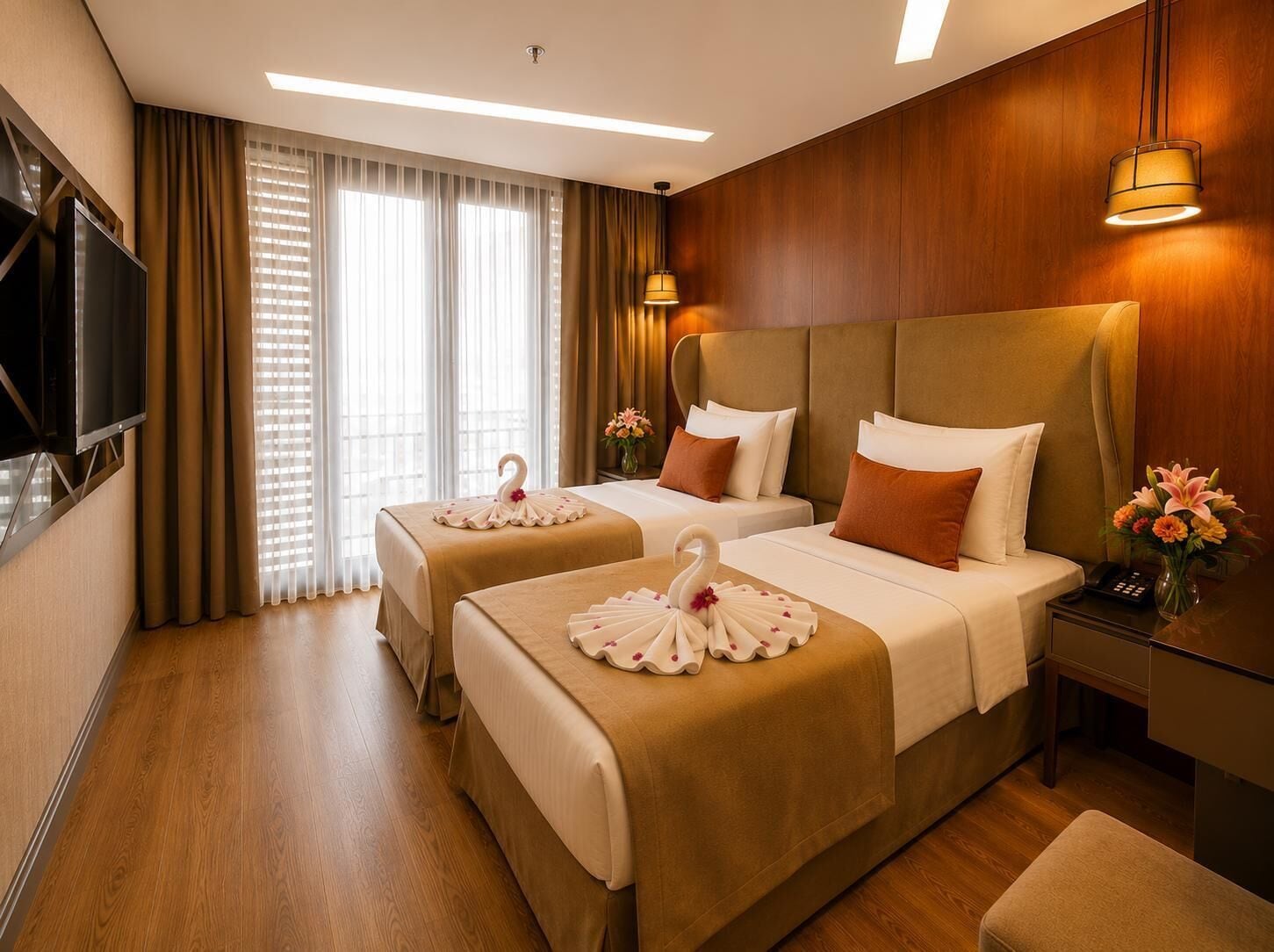 A hotel room with two beds, a TV, a bedside table with a vase of flowers, and a window with curtains.