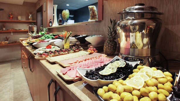 Un buffet proposant une variété d’aliments, notamment du jambon, des olives, des citrons et un grand récipient en argent.