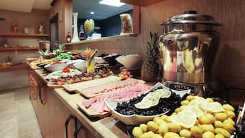 Un bufé con distintos alimentos, entre ellos jamón, aceitunas, limones y un recipiente plateado grande.