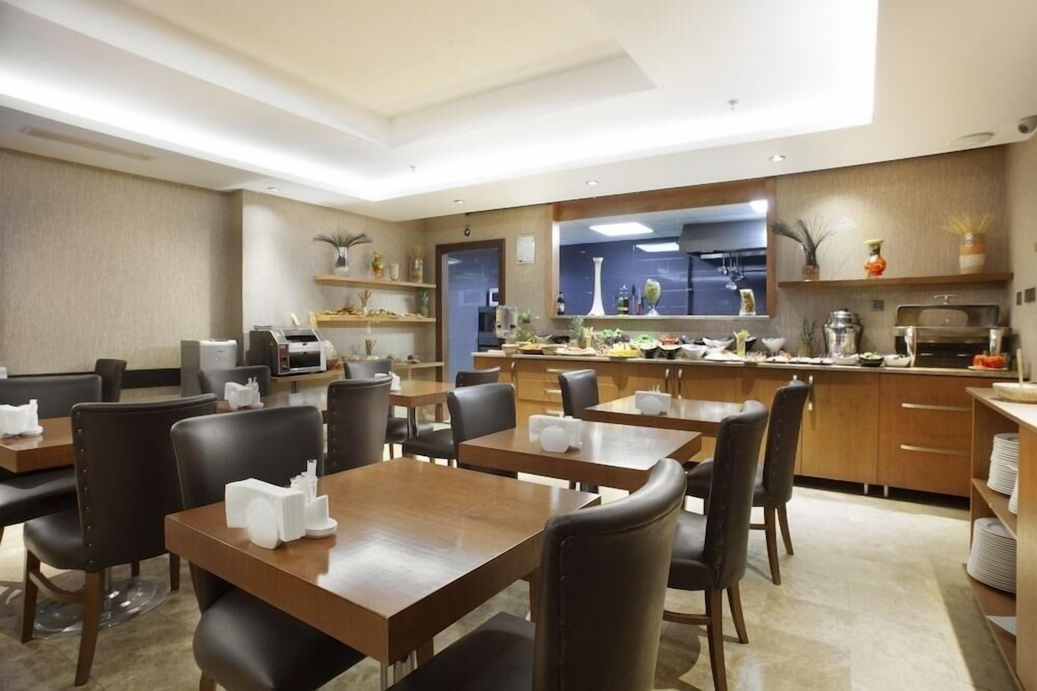 A restaurant with wooden tables and chairs, a kitchen area, and shelves with decorative items.