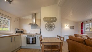 A kitchen with a dining table and chairs, a microwave, oven, and a clock on the wall. - Ash Tree Lodge - sleeps 4 guests in 2 bedrooms (Appin)