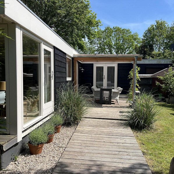 Uma casa moderna com um pátio, área de refeições com mobiliário de exterior e um jardim com vasos de plantas.