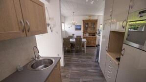 Een keuken met houten kastjes, een roestvrijstalen spoelbak en een eethoek met rieten stoelen.