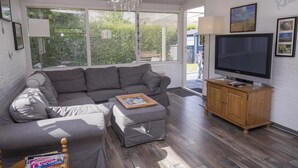 Een woonkamer met een grijze modulaire bank, een houten tv-meubel en een kroonluchter.