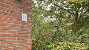Un muro in mattoni con un piccolo cartello, fitta vegetazione e alberi sullo sfondo.