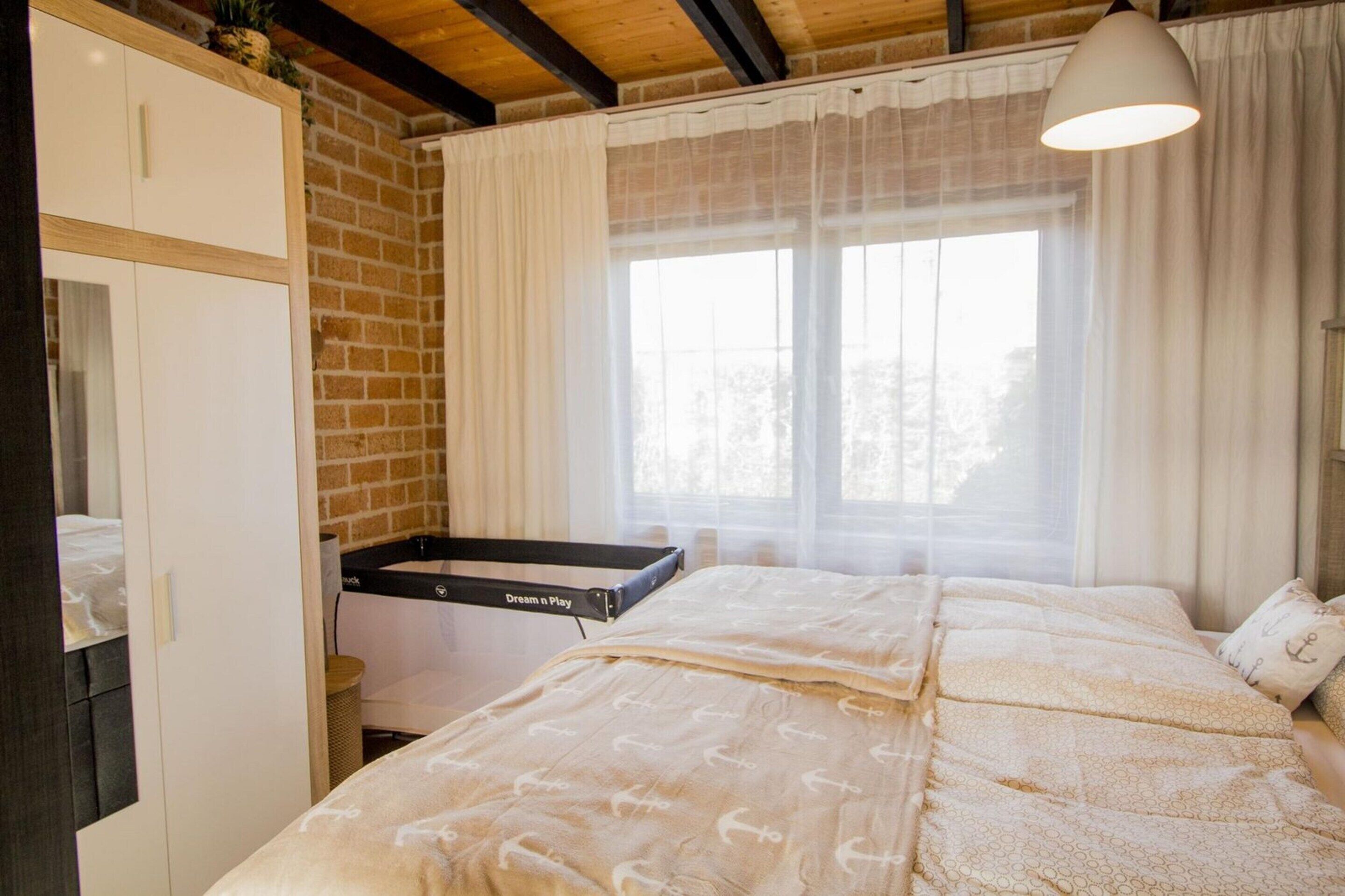 A bedroom with a bed, a wardrobe, a desk with a lamp, and a window with curtains.