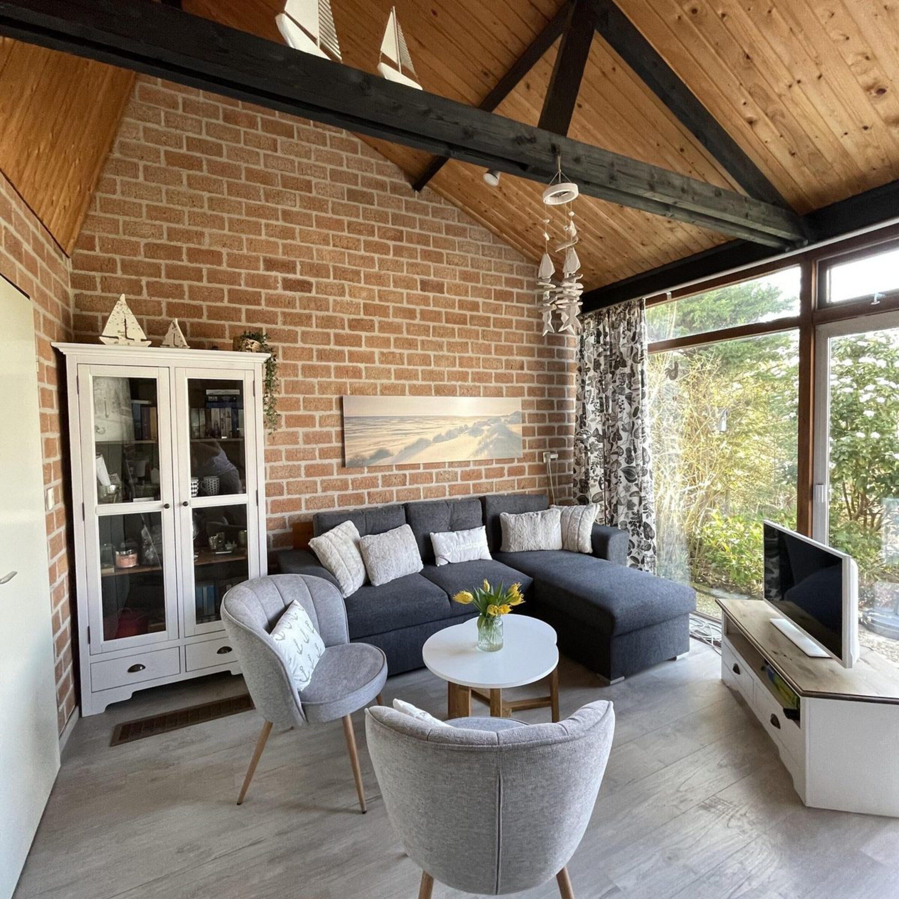 A cozy living room with a brick wall, a sectional sofa, a white cabinet, and a TV.