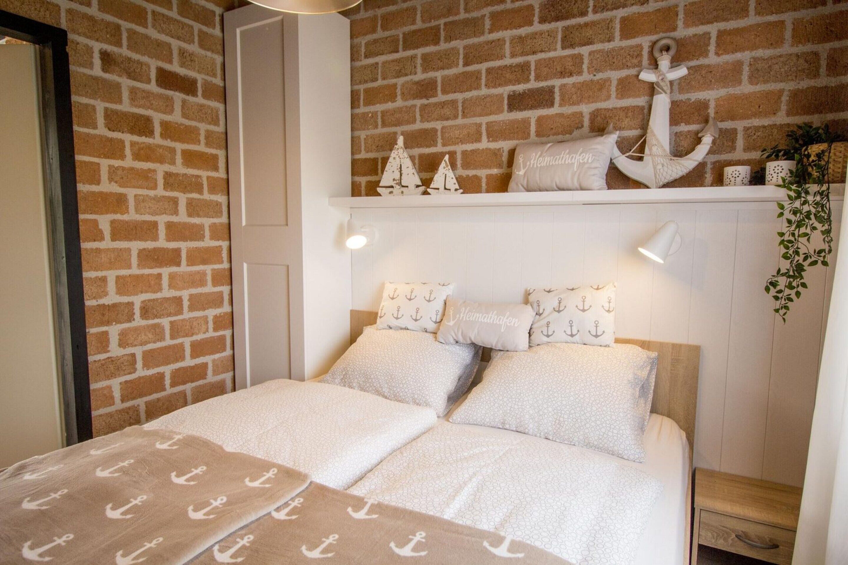 A bedroom with a brick wall, a bed with white bedding, and a shelf with decorative items.