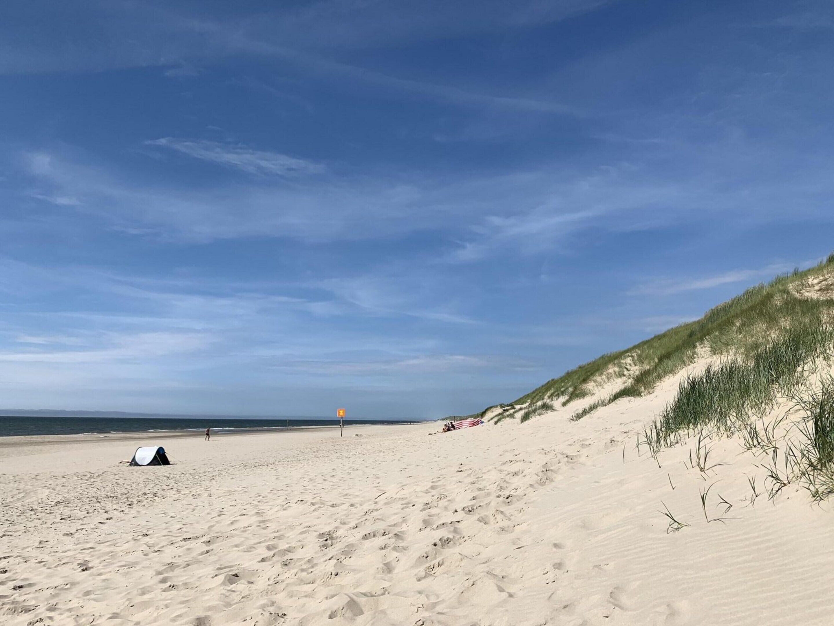 En strand med ett tält, en sanddyn och en flagga.