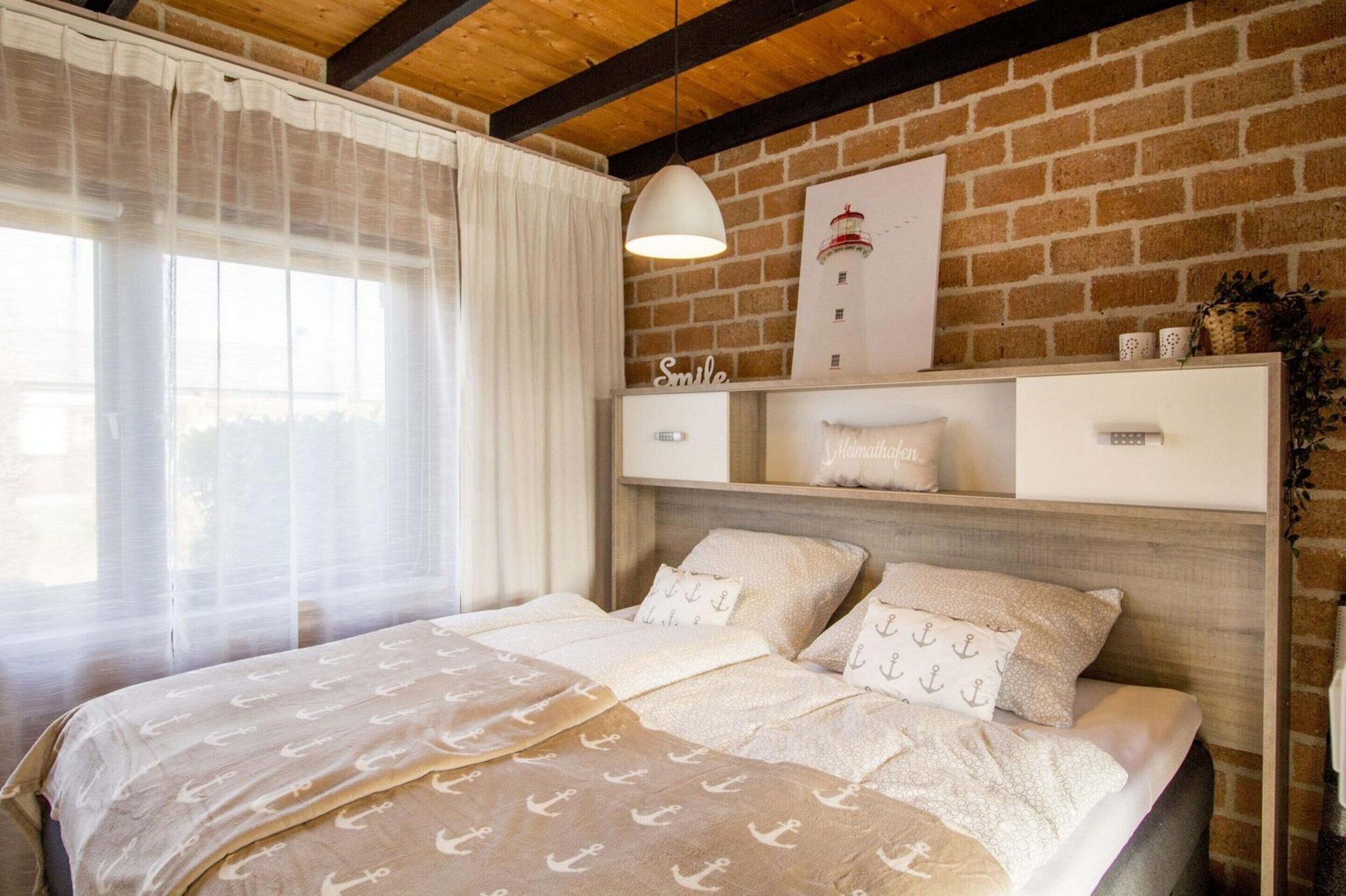 A bedroom with a bed, a hanging light, a brick wall, and a shelf with decorative items.