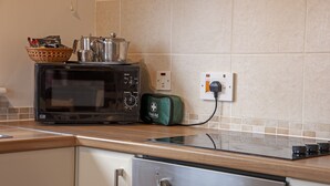 A kitchen with a microwave, a toaster, and a kettle on the counter. There is a basket with utensils and a green bag with a white cross. - Birch Tree Lodge - sleeps 4 guests in 2 bedrooms (Appin)