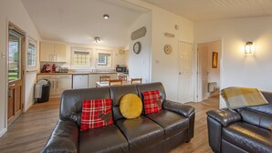 A spacious living area with a leather sofa, a dining table, and a kitchen in the background. - Birch Tree Lodge - sleeps 4 guests in 2 bedrooms (Appin)
