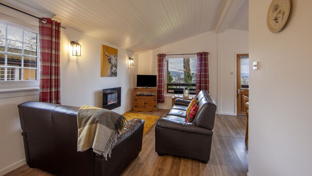 A living room with a fireplace, two sofas, a television, and a large window with curtains. - Birch Tree Lodge - sleeps 4 guests in 2 bedrooms (Appin)