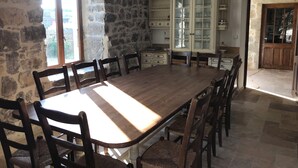 Un comedor con una gran mesa de madera y sillas, paredes de piedra y vistas a través de un ventanal.