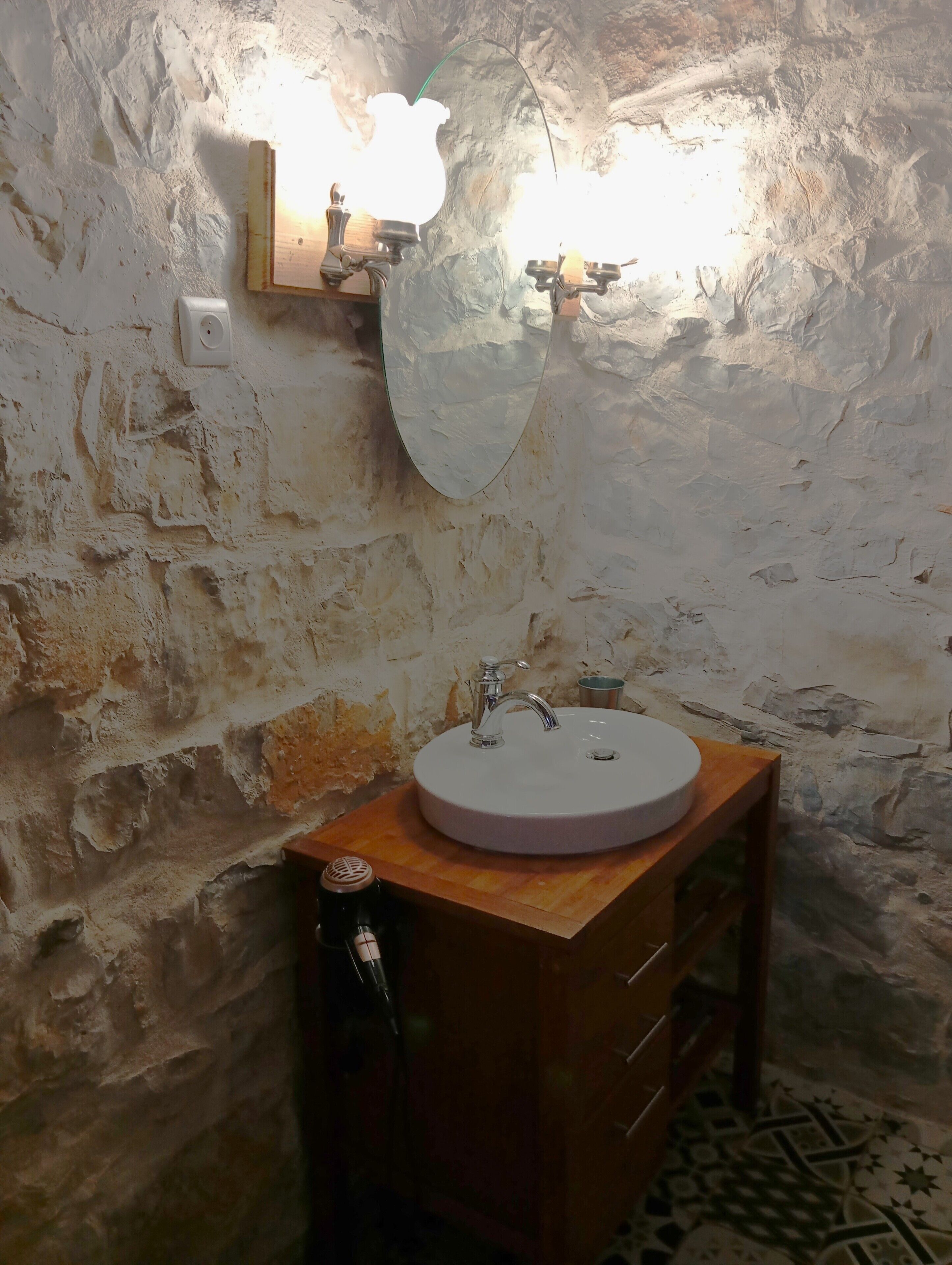 Un bagno con parete in pietra, un mobile lavabo in legno, un lavandino rotondo e uno specchio.