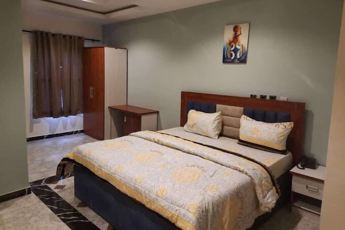 A hotel room with a bed, a nightstand, a wardrobe, and a painting on the wall.