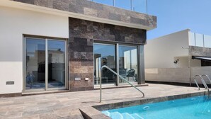 A modern building with a swimming pool, large glass doors, and a stone facade. - 10min from the beach, Villa 2023 with Swimming Pool, Terrace, Roof-Terrace, Parking  (Orihuela)