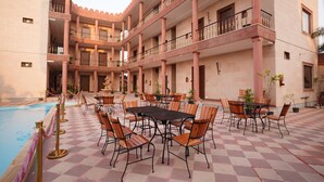 A courtyard with a pool, multiple dining tables and chairs, and a multi-story building with balconies. - HOTEL THE FORT (Amroha)