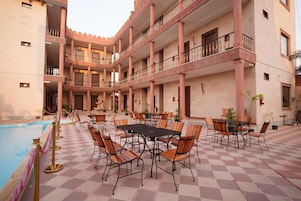 Un patio con piscina, varias mesas y sillas de comedor, y un edificio de varios pisos con balcones.