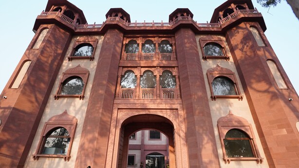 A large, historic building with a grand entrance, multiple arched windows, and two cannons at the front. - HOTEL THE FORT (Amroha)