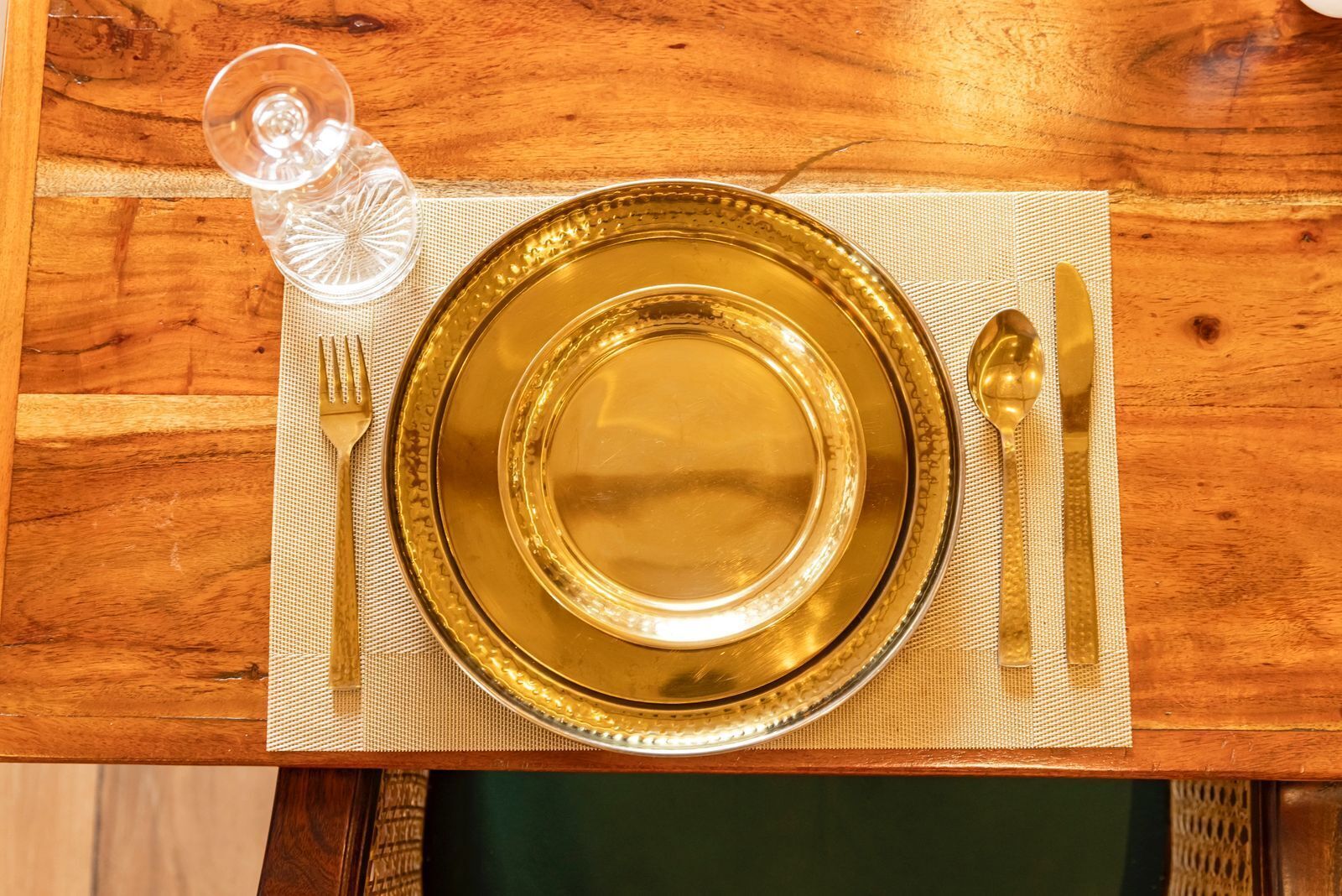 A table set with a gold-rimmed plate, a fork, a knife, and a spoon on a placemat.