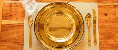 A table set with a gold-rimmed plate, a fork, a knife, and a spoon on a placemat.