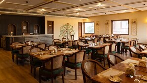 A restaurant with multiple dining tables and chairs, a bar area, and a decorative tree mural on the wall. - HOTEL THE FORT (Amroha)